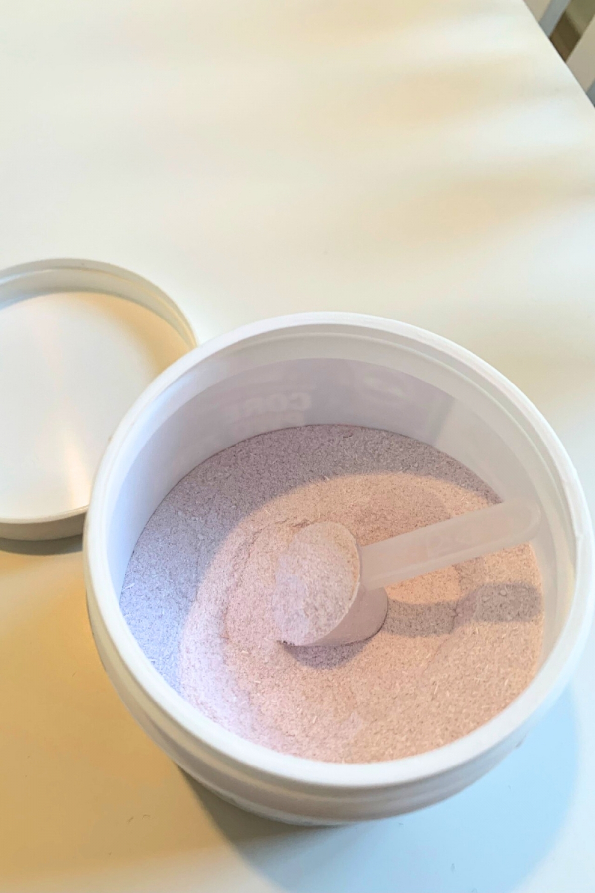 Öppen burk med ljusrosa pulver och skopa fotograferad av oss